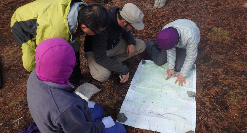 Four people examine a map that is spread out on the ground. 